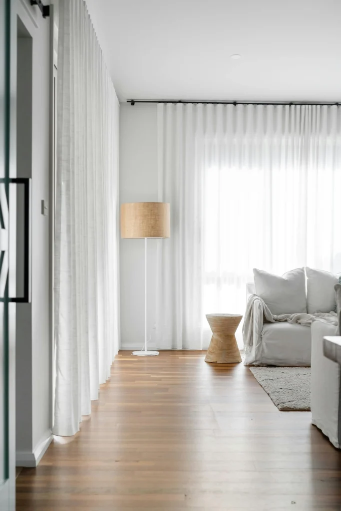 Vista de vivienda en tonos neutros con suelo de madera, enfocando a lampara blanca y beige y con una mesa de madera en forma de diábolo